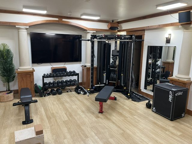 Luxury home gym with functional trainer, dumbbell rack, and a wall-mounted display between columns