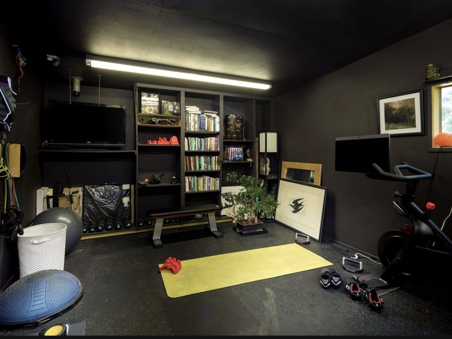Home gym built into a media room, with a bike, mat, and wall-mounted straps